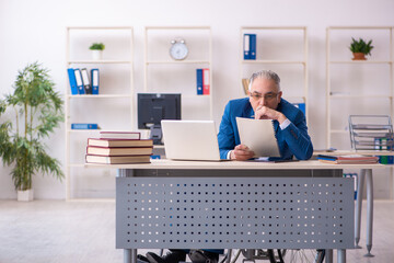 Old male employee in wheel-chair sitting in the office