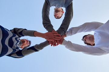 A low angle shot of three young friends putting their hands together against a blue sky