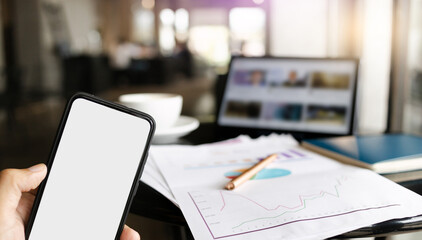 Close up of blank screen mobile in hand, businessman working online with paperwork and digital tablet