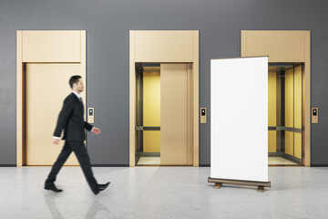 Wall Mural - businessman walking in grey concrete interior with three elevator doors and empty mockup poster. opp