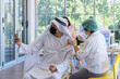© godji10 - Arab people use mobile phone taking selfie while Asian doctor use syringe to injecting covid-19 vaccine in the hospital to prevent outbreak of coronavirus. Immunization, Covid-19 vaccination clinic.