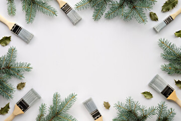 Frame, brushes with Christmas tree twigs, natural fir twigs and holly leaves. Creative simple minimal winter background. Winter time DIY renovation flat lay, top view in cool natural green shades.