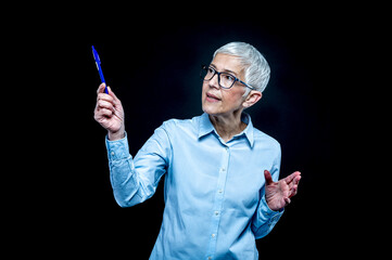 Aged, short-haired, Caucasian woman with a blue shirt and glasses holding a pen.