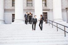 Four Well Dressed Professionals Walk Down Steps In Discussion Outside Of A Courthouse Or Municipal Building.. Could Be Lawyers, Business People Etc.