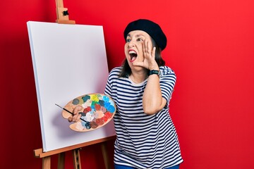 Sticker - Middle age hispanic woman standing drawing with palette by painter easel stand shouting and screaming loud to side with hand on mouth. communication concept.