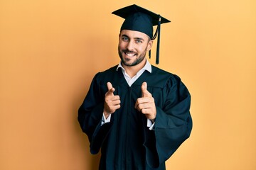 Sticker - Young hispanic man wearing graduation cap and ceremony robe pointing fingers to camera with happy and funny face. good energy and vibes.