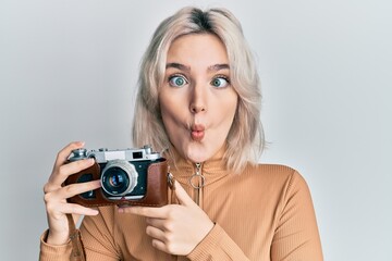 Sticker - Young blonde girl holding vintage camera making fish face with mouth and squinting eyes, crazy and comical.