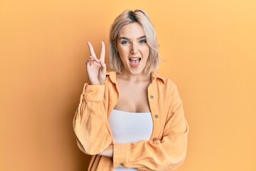 Sticker - Young blonde girl wearing casual clothes smiling with happy face winking at the camera doing victory sign. number two.