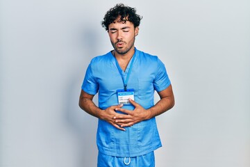 Sticker - Young hispanic man wearing blue male nurse uniform with hand on stomach because indigestion, painful illness feeling unwell. ache concept.