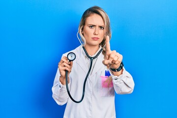 Sticker - Beautiful young blonde doctor woman holding stethoscope pointing with finger up and angry expression, showing no gesture