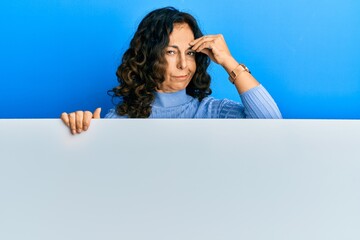 Sticker - Middle age hispanic woman holding blank empty banner worried and stressed about a problem with hand on forehead, nervous and anxious for crisis