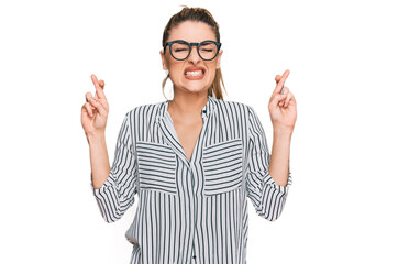 Young caucasian woman wearing business shirt and glasses gesturing finger crossed smiling with hope and eyes closed. luck and superstitious concept.