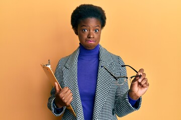 Poster - Young african american girl holding clipboard and glasses puffing cheeks with funny face. mouth inflated with air, catching air.