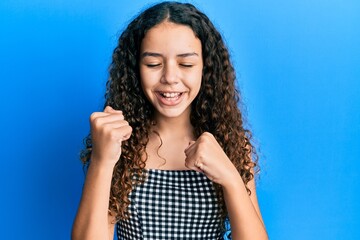 Wall Mural - Teenager hispanic girl wearing casual clothes celebrating surprised and amazed for success with arms raised and eyes closed