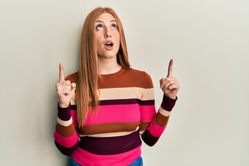 Young irish woman wearing casual clothes amazed and surprised looking up and pointing with fingers and raised arms.