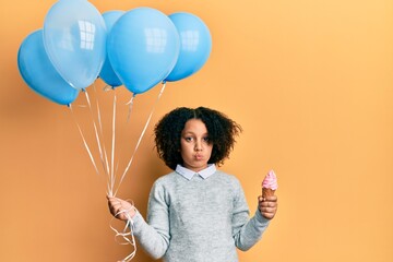 Sticker - Young little girl with afro hair holding ice cream and blue balloons looking at the camera blowing a kiss being lovely and sexy. love expression.