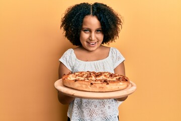 Poster - Young little girl with afro hair holding italian pizza smiling and laughing hard out loud because funny crazy joke.