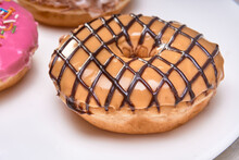 Maple Glazed Doughnut With A Chocolate Grid On A White Plate With A Marble Background. Close-up View