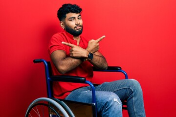 Canvas Print - Arab man with beard sitting on wheelchair pointing to both sides with fingers, different direction disagree