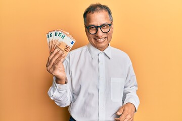 Wall Mural - Middle age indian man holding bunch of 50 euro banknotes looking positive and happy standing and smiling with a confident smile showing teeth