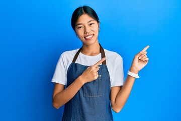 Sticker - Young chinese woman wearing waiter apron smiling and looking at the camera pointing with two hands and fingers to the side.