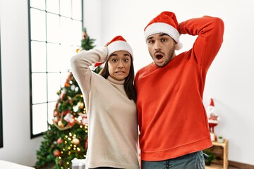 Canvas Print - Young hispanic couple standing by christmas tree crazy and scared with hands on head, afraid and surprised of shock with open mouth