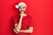 © Krakenimages.com - Young hispanic man wearing christmas hat looking confident at the camera with smile with crossed arms and hand raised on chin. thinking positive.