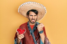 Young Hispanic Man Wearing Mexican Hat Holding Chili Annoyed And Frustrated Shouting With Anger, Yelling Crazy With Anger And Hand Raised