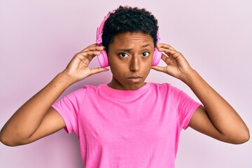 Wall Mural - Young african american girl listening to music using headphones skeptic and nervous, frowning upset because of problem. negative person.