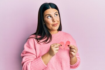 Sticker - Beautiful brunette woman holding broken heart paper shape smiling looking to the side and staring away thinking.