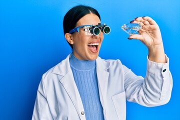 Poster - Beautiful brunette jeweller woman holding brilliant diamond stone wearing magnifier glasses smiling and laughing hard out loud because funny crazy joke.