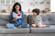 © DimaBerlin - Excited young mom positive emotional reading greetings from card made by preschooler child son sitting near happy proud mum on sofa at mother day or birthday morning congratulating parent with holiday