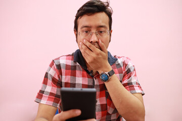 Wall Mural - Indian man covering his mouth showing a shocking gesture while using a smartphone