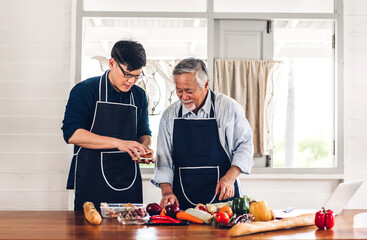 Wall Mural - Portrait of happy love asian family senior mature father and young adult son having fun cooking together and looking for recipe on Internet with laptop computer to prepare the yummy eating lunch