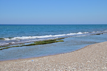 The surf on the pebble beach. Blue cloudless sky