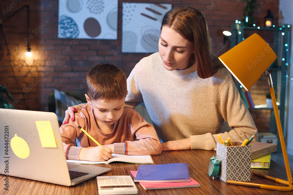 Little boy with his mother doing homework at home late in evening