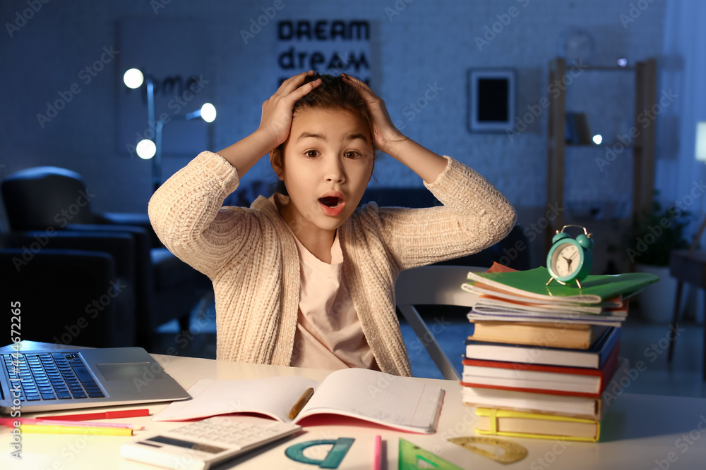 Shocked little girl doing homework at home late in evening