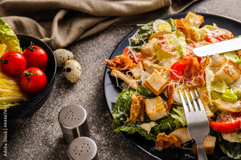 Plate with tasty Caesar salad and ingredients on grunge background, closeup
