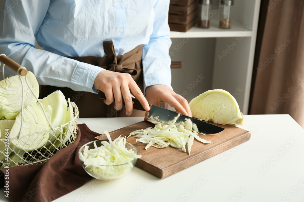 Woman cutting fresh cabbage on table in kitchen, closeup
