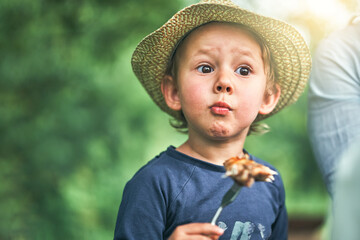 Surprised little boy eats grilled chicken wing in park