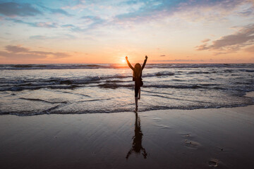 Wall Mural - young girl jumping for happiness on the beach at sunset