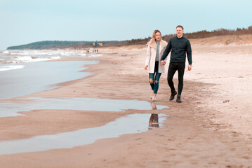 Attractive young couple walking along the shore of a sandy beach, on a spring romantic holiday, outdoors.