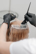 Girl in a beauty salon. A craftsman in black gloves smears paint on the hairs. hair dyeing services.