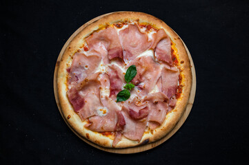 Pizza with tomato sauce, mozzarella and ham on a black background.