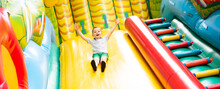 Little Boy Child Rides On An Inflatable Multi-colored Slide.