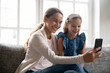 © fizkes - Smiling young Caucasian mother and little daughter relax at home have fun talk speak on video call on cellphone. Happy mom and small girl child enjoy having webcam digital virtual event on smartphone.