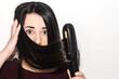 © AliciaFdez - Close-up of a beautiful young woman with long black shiny hair looking surprised while using a flat iron. Girl in shock with a hand in her head. Hair straightener