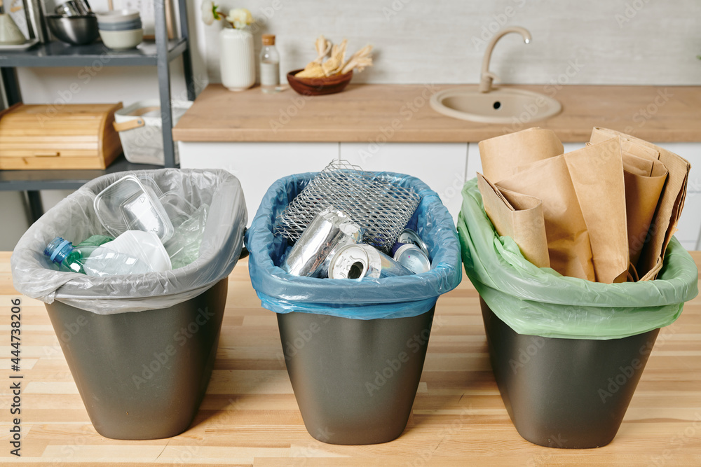 Row of three trash bins with sorted garbage on kitchen table - obrazy, fototapety, plakaty 