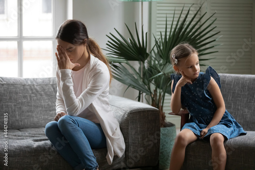 Unhappy young Caucasian mother and small teen daughter sit separately back to back after family quarrel. Upset sad mom and little girl child avoid ignore talking after fight. Generation gap concept.