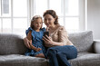 © fizkes - Loving modern old Caucasian grandmother and little granddaughter sit on sofa at home talk speak on video call on smartphone. Smiling granny and small grandchild use cellphone browse internet.